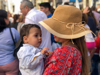 Woman with brown hat in the street, with her son in her arms. her son looks at her with tenderness 