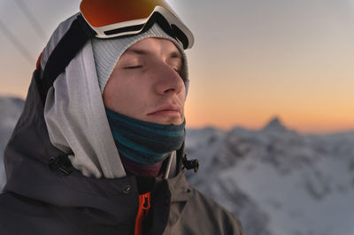 Close up portrait of happy young man in cold weather in winter mountains at sunset. the face of a