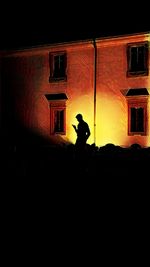 Silhouette man standing against illuminated building at night