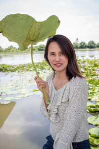 Portrait of smiling woman holding leaf by water