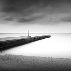 Pier at beach against sky during foggy weather