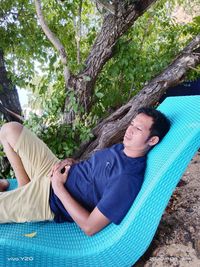 Young man lying on hammock against tree trunk