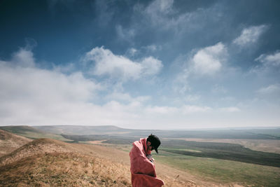 Side view of woman standing on landscape against sky