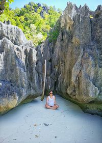 Woman sitting against rock formations at beach