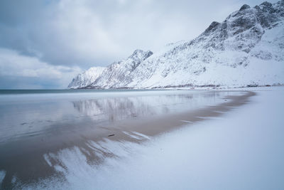 Scenic view of sea by snowcapped mountain against sky