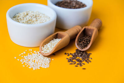 Wooden spoons with sesame and flax seeds lies in a white mortar on a yellow background. healthy eat