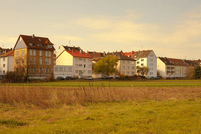 Houses on field by buildings in town against sky