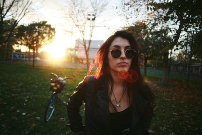 Portrait of smiling young woman wearing sunglasses against sunset sky