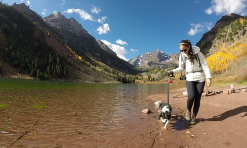 Woman walking with cavalier king charles spaniel on lakeshore against mountains