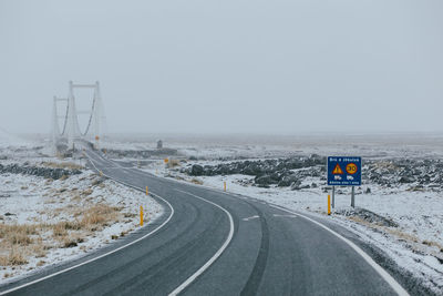 Road passing through snow covered landscape against clear sky