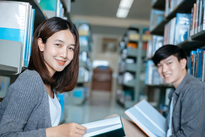 Portrait of smiling friends with book sitting in library