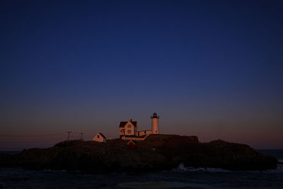 Lighthouse by sea against clear sky during sunset