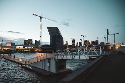 Illuminated buildings by sea against sky at dusk