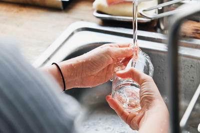 Cropped image of person washing glass in sink