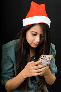 Close-up of beautiful woman holding camera while standing against black background