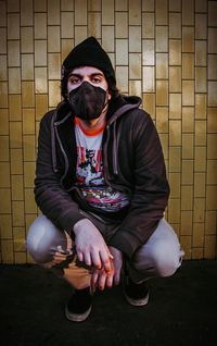 Portrait of young man sitting against wall