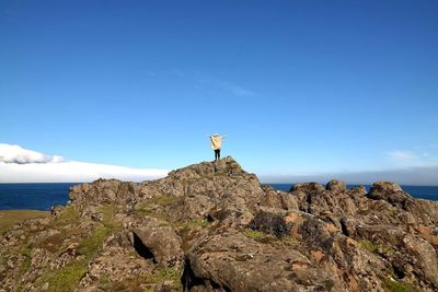 Man standing on rock by sea against clear blue sky