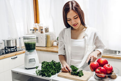 Smiling young woman cutting vegetables on table