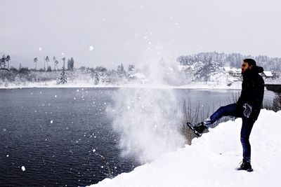 Full length of man kicking snow in river against cloudy sky