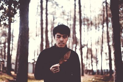 Young man holding leaf while standing in forest