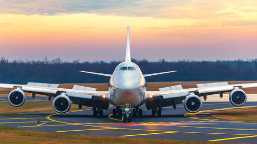 Airplane on runway against sky during sunset