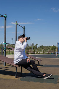 . young sportive woman in sport clothes drinking water from thermos bottle on sport ground