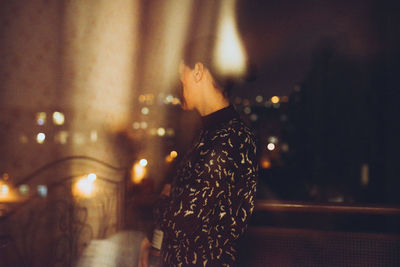 Side view of woman standing by railing seen through glass window at night