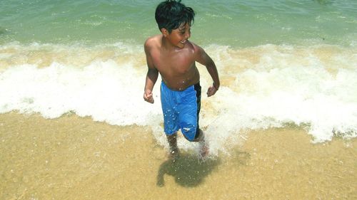 High angle view of shirtless boy enjoying on shore at beach