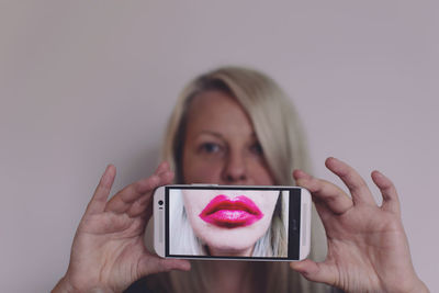 Close-up of woman holding smart phone with pink lips on display against white background