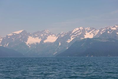 Scenic view of sea by snowcapped mountain against sky