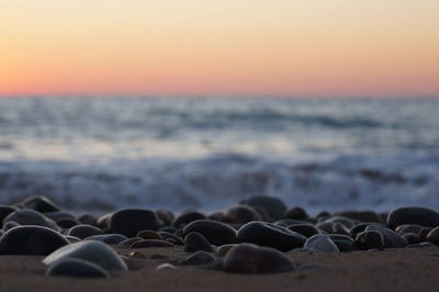 Stones on beach against sea during sunset