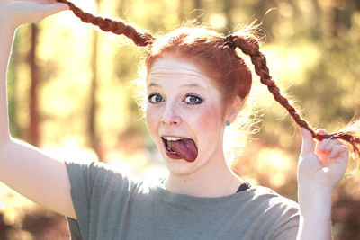 Portrait of woman holding braided hair while sticking out tongue