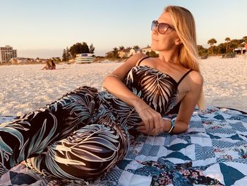 Young woman with sunglasses  sitting  at beach against sky