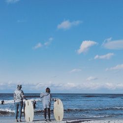 Rear view of people with surfboard standing on shore at beach