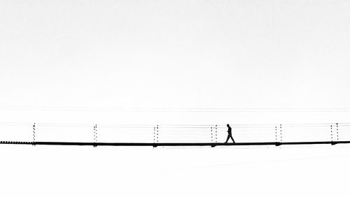 Silhouette person walking on footbridge against clear sky