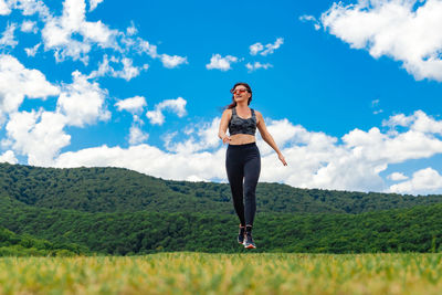 Young woman standing on field against sky
