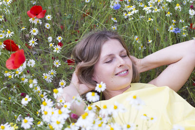 A beautiful young blonde woman in a yellow dress stands among a flowering field