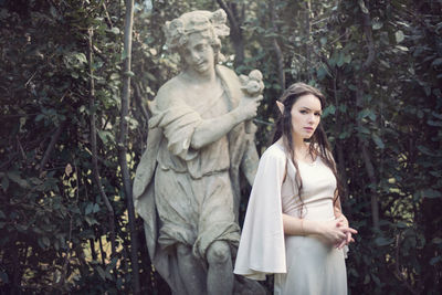 Young woman standing by statue in forest