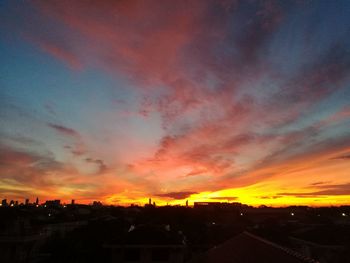 Silhouette houses against dramatic sky during sunset