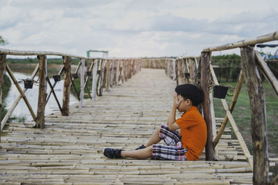 Side view of boy sitting on wooden footbridge