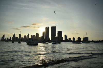 Silhouette of city at waterfront during sunset