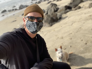Portrait of man wearing sunglasses on beach with his dog