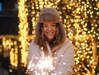 Smiling young woman holding sparkler against christmas decoration
