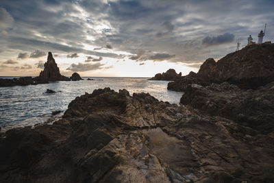 Rock formation at beach against cloudy sky during sunset