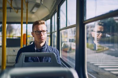 Man listening music on headphones while sitting by window in bus