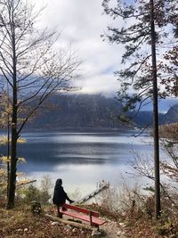 Rear view of woman sitting by lake against sky