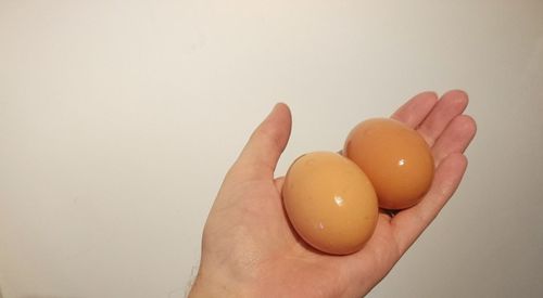 Cropped image of hand holding eggs against beige wall