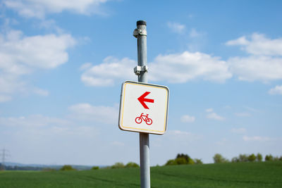 Road sign on field against sky