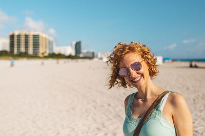 Portrait of young woman wearing sunglasses standing at beach