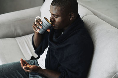 Full length of man wearing hat sitting on sofa at home